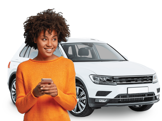 Brown haired brown woman in orange top smiling and looking to side with a phone in her hands. White SUV car in the background.